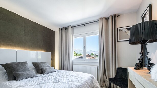 Un dormitorio moderno con una cama grande, un escritorio con lámpara y vistas a las montañas a través de la ventana.