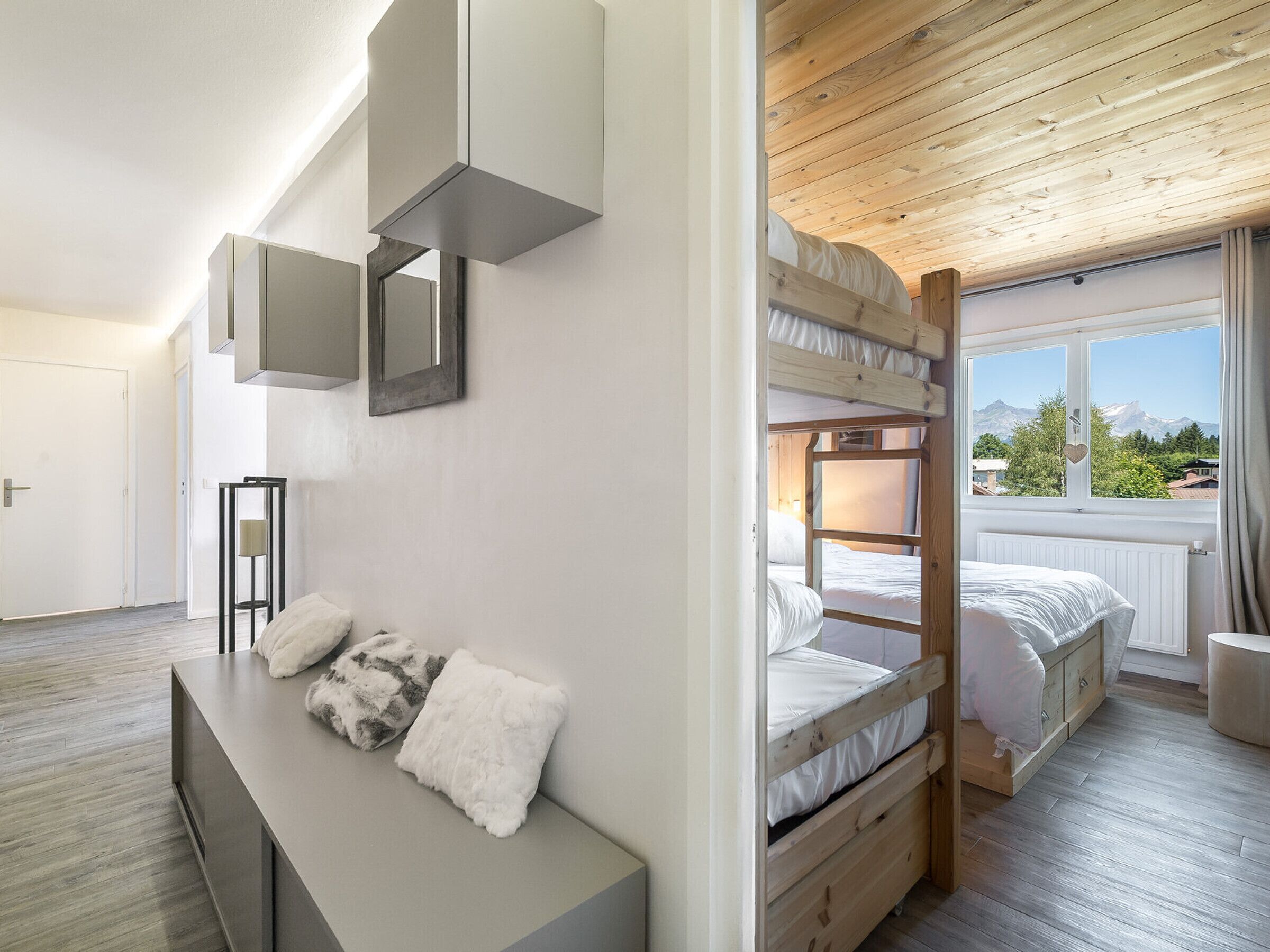 Una camera da letto moderna con letti a castello, un comodino con cuscini decorativi, un'ampia finestra con vista sulle montagne e un soffitto in legno.
