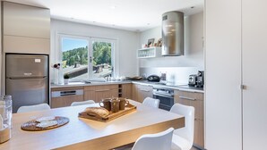 Una cocina moderna con un ventanal amplio, electrodomésticos de acero inoxidable y una zona de comedor con sillas blancas.