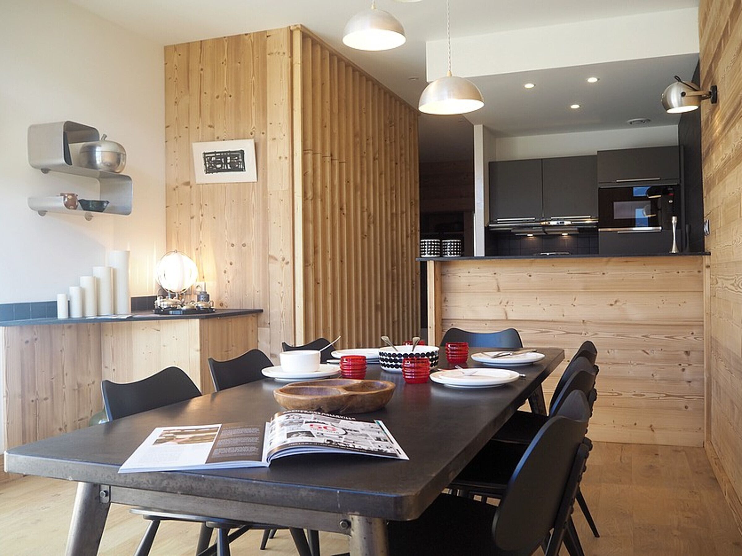 Un comedor con un separador de madera, una cocina al fondo y una revista sobre la mesa.