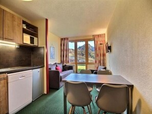 Cocina compacta con zona de comedor, sofá y vistas a montañas a través de una ventana.