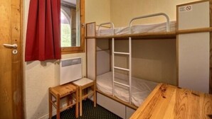 Ein kleiner, kompakter Raum mit einem Etagenbett, einem kleinen Holztisch und einem Fenster mit rotem Vorhang.