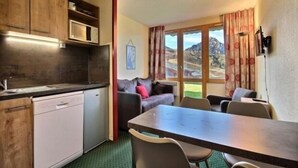 Eine kompakte Küche mit Geschirrspüler, einem Esstisch mit Stühlen und einer Couch.