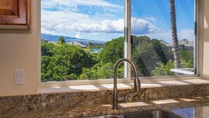 A kitchen with a large window overlooking a lush landscape and a clear sky.
