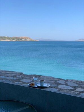 Une table avec une tasse et une soucoupe, un verre et une pâtisserie, le tout posé sur une corniche en pierre donnant sur une étendue d’eau.
