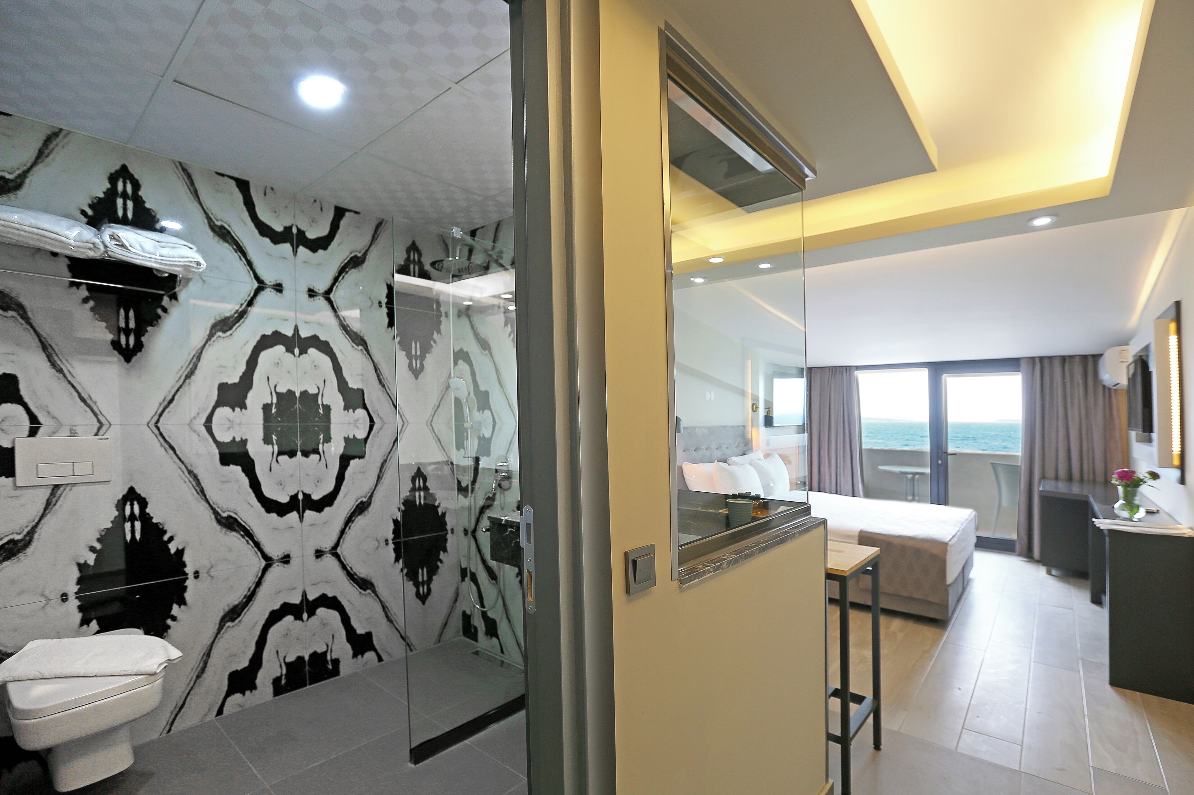 Habitación de hotel moderna con baño que presenta un revestimiento con diseño, una cama, un escritorio y vista al mar.