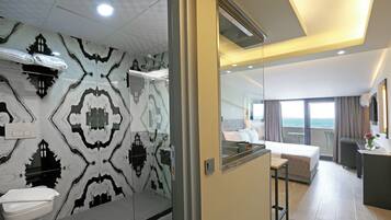 Habitación de hotel moderna con baño que presenta un revestimiento con diseño, una cama, un escritorio y vista al mar.