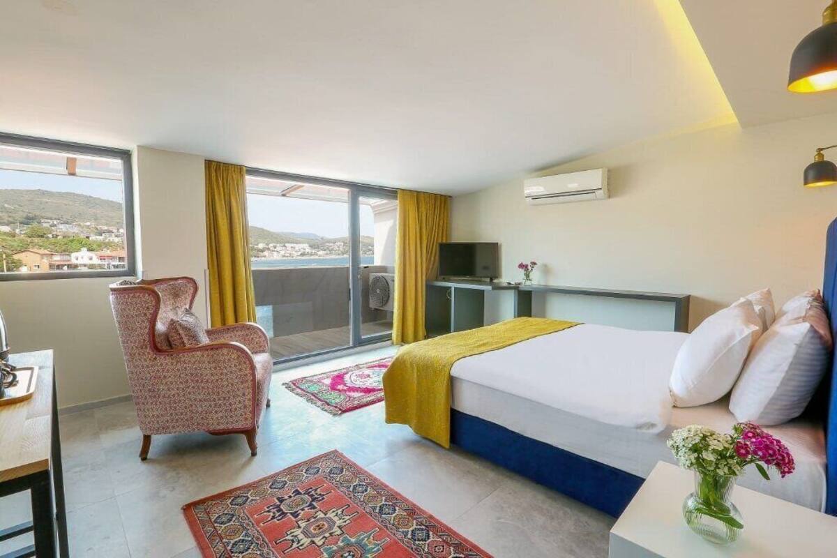 Habitación de hotel con cama, una silla, un escritorio, televisor y balcón con vistas.