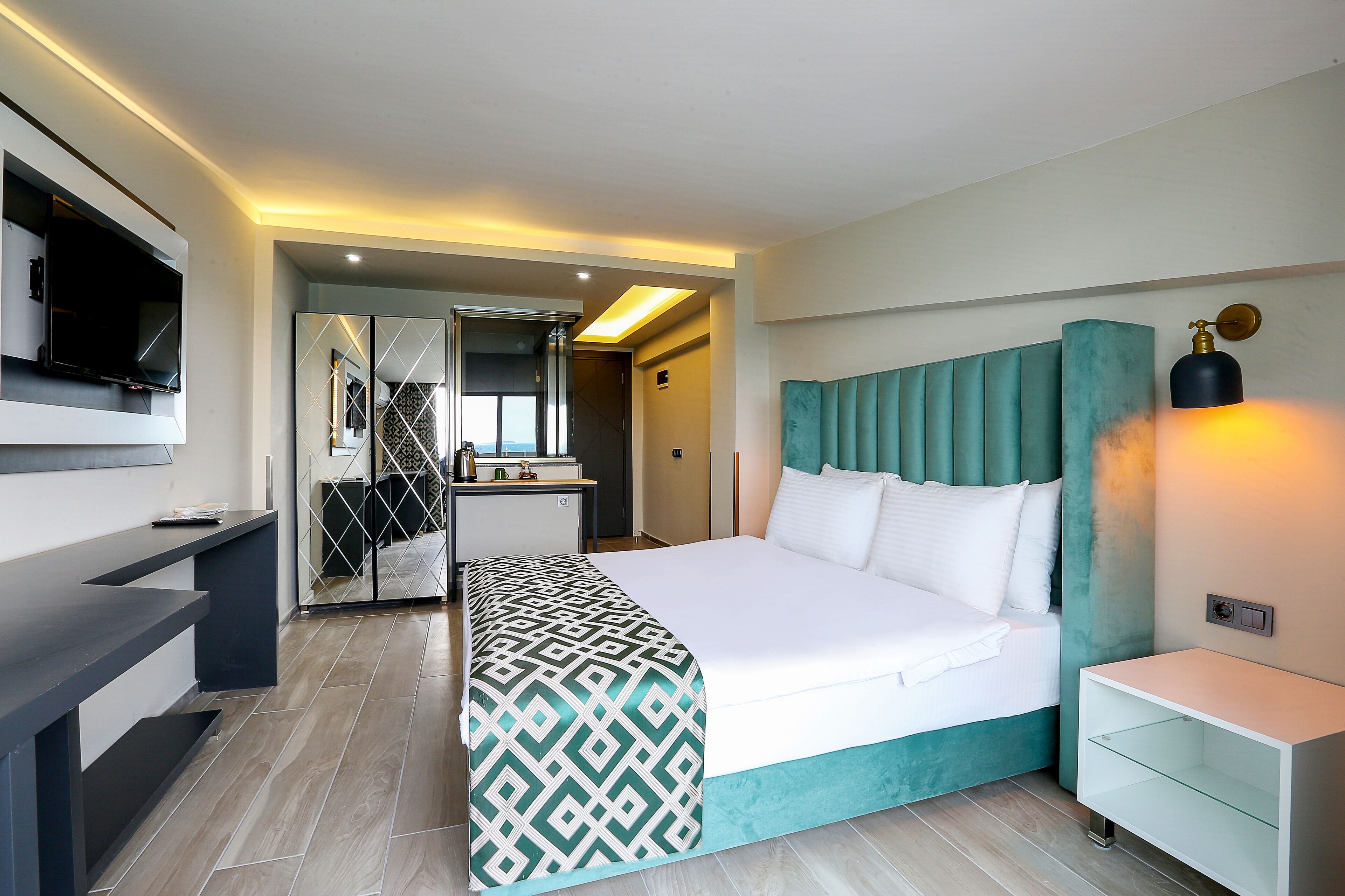 A modern hotel room with a bed, a TV, a desk, and a bathroom visible through an open door.