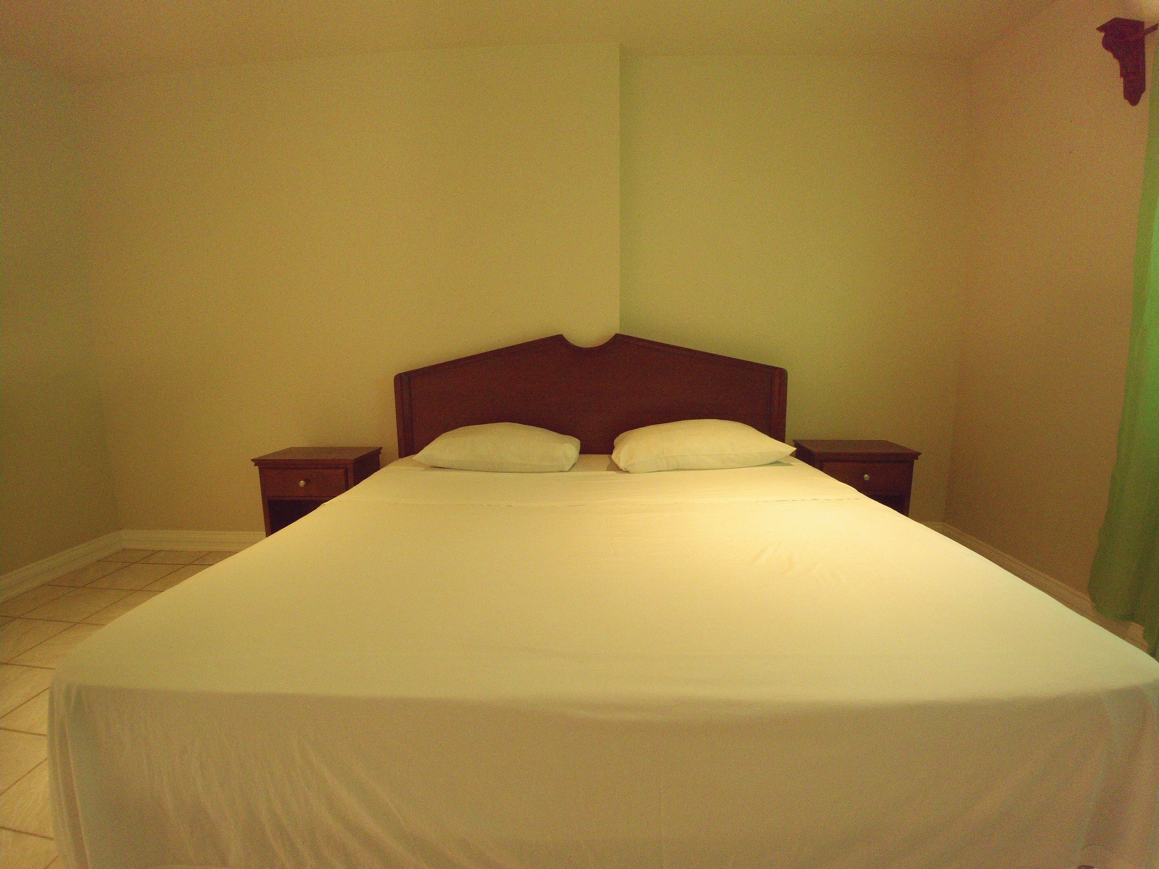 A single bed with a wooden headboard in a room with plain walls and a tiled floor.