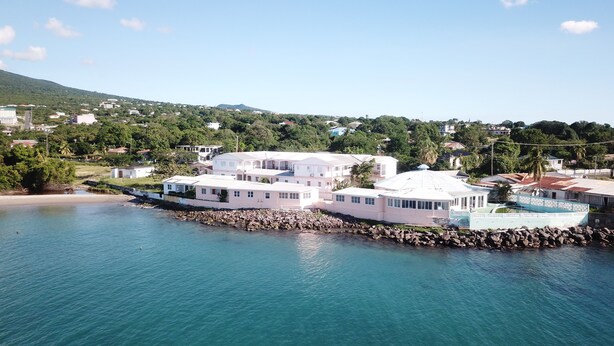 A coastal area with a large white building complex by the water, surrounded by greenery and residential buildings. - Pinneys Beach Hotel Nevis (Charlestown)