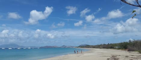A beach with a clear sky, calm sea, and distant mountains.