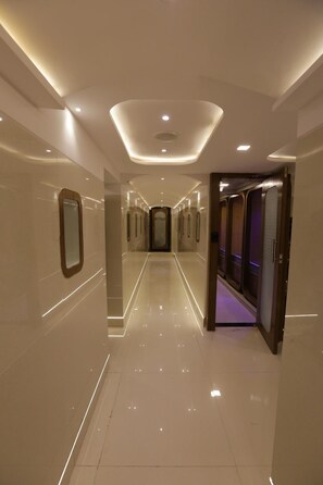 A modern hotel corridor with a polished floor, recessed lighting, and a central elevator.