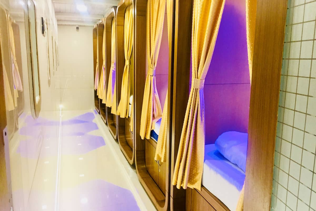 A row of wooden bunk beds with curtains, a tiled floor, and a purple-lit ceiling.