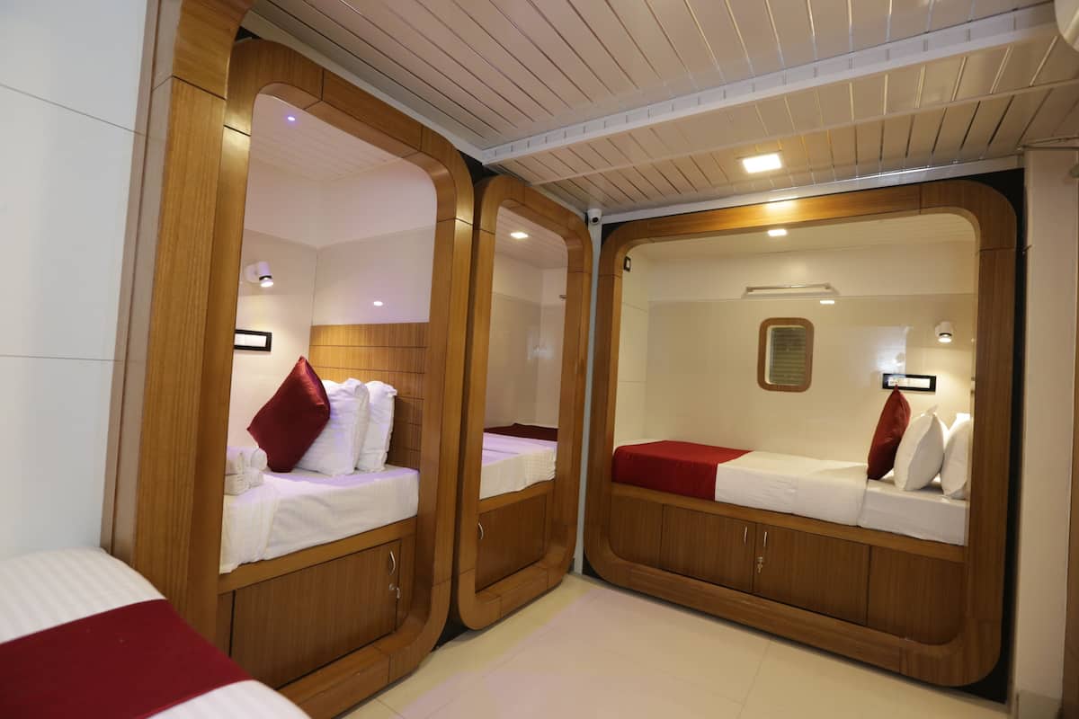 A compact, well-lit room with two wooden bunk beds, each with a pillow and a small bedside table.