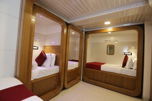 A compact, well-lit room with two wooden bunk beds, each with a pillow and a small bedside table.