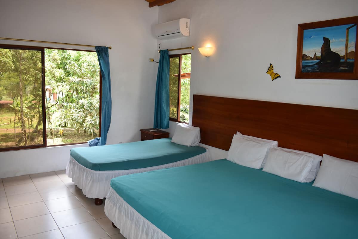 Una habitación con dos camas, una ventana con cortinas, una mesita de noche y un aire acondicionado de pared.