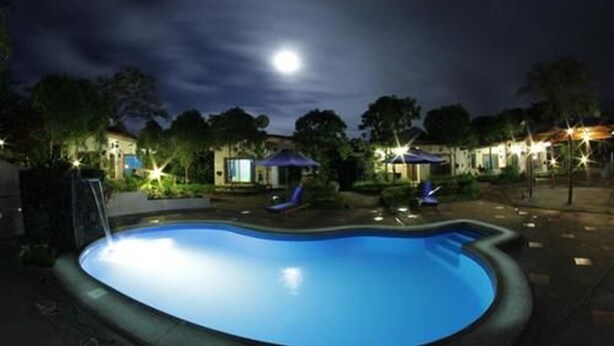 A swimming pool at night with surrounding lounge chairs and umbrellas, under a dark sky with a visible moon. - Piedras Blancas Lodge (Bella Vista)