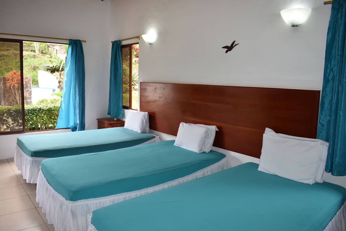 Habitación de hotel con dos camas, cabecero de madera, mesita de noche y ventana con cortinas.