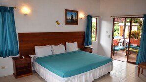 A bedroom with a large bed, wooden headboard, two bedside tables, and a view of the outside through a sliding glass door. - Piedras Blancas Lodge (Bella Vista)