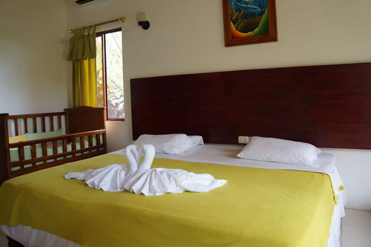 Habitación de hotel con cama, cabecera de madera, colcha amarilla, almohadas blancas y un cuadro en la pared.