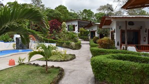 A pathway leading to a house with a satellite dish, surrounded by well-maintained hedges and a small pool. - Piedras Blancas Lodge (Bella Vista)