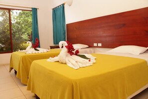 Hotelkamer met twee bedden, elk met een gele sprei en een handdoek in de vorm van een zwaan. Er is een raam met gordijnen, een houten hoofdeinde en een nachtkastje met een lamp.