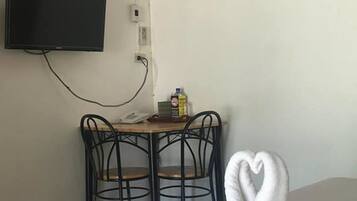 A hotel room with a bed, a TV mounted on the wall, a desk with a chair, and a bottle of water on the desk.