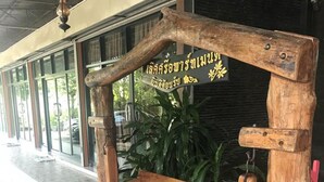 A wooden bench with a sign in a foreign language, placed on a tiled floor with a glass door in the background. - Lert Sri Hotel (Suphan Buri)