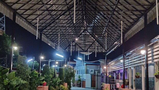 An indoor corridor with a tiled floor, metal ceiling, and potted plants along the sides. - Jumbo Villa Homestay and Resort (Wiset Chai Chan)