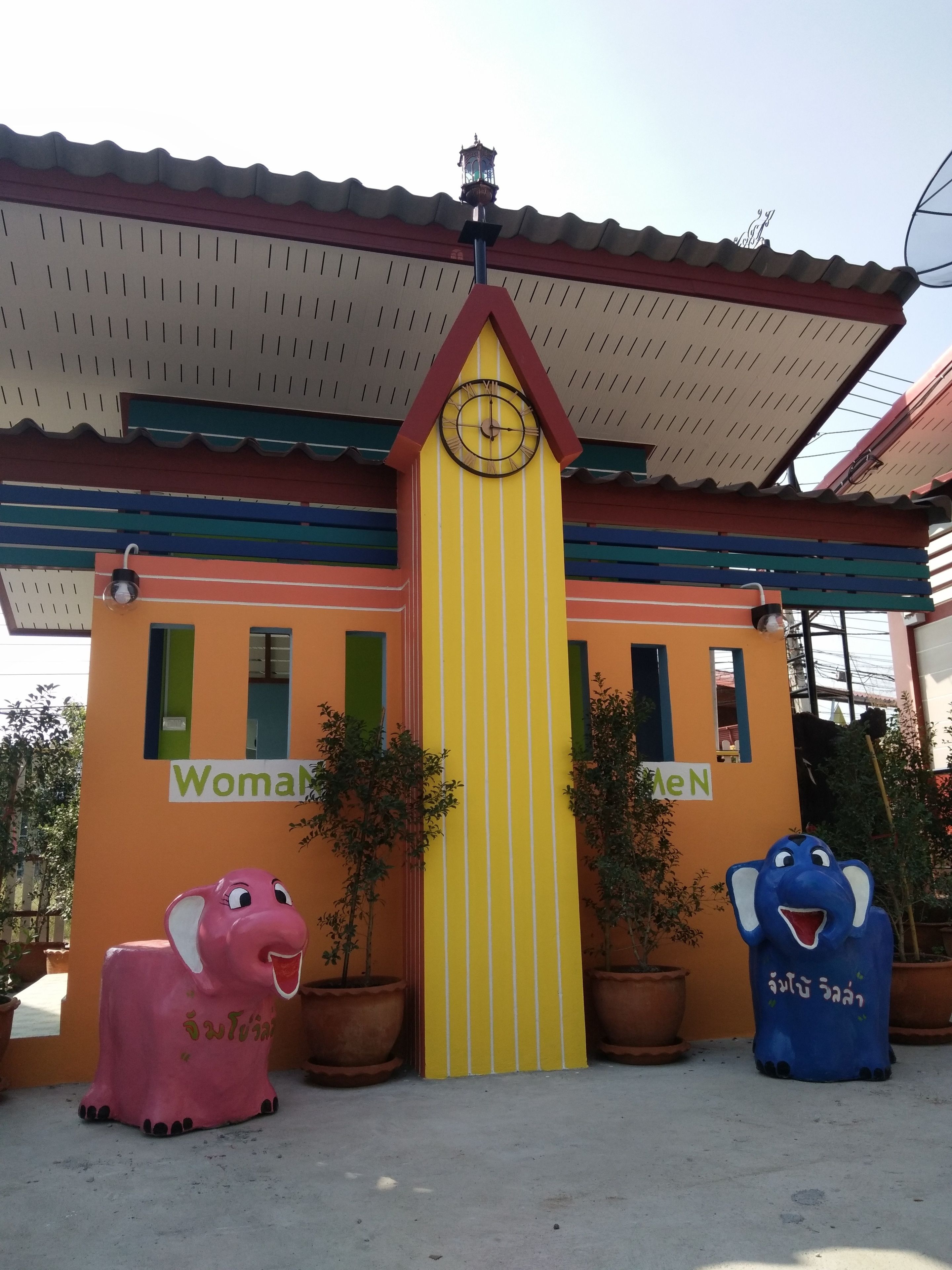 A colorful building with a clock, two potted plants, and two animal statues.
