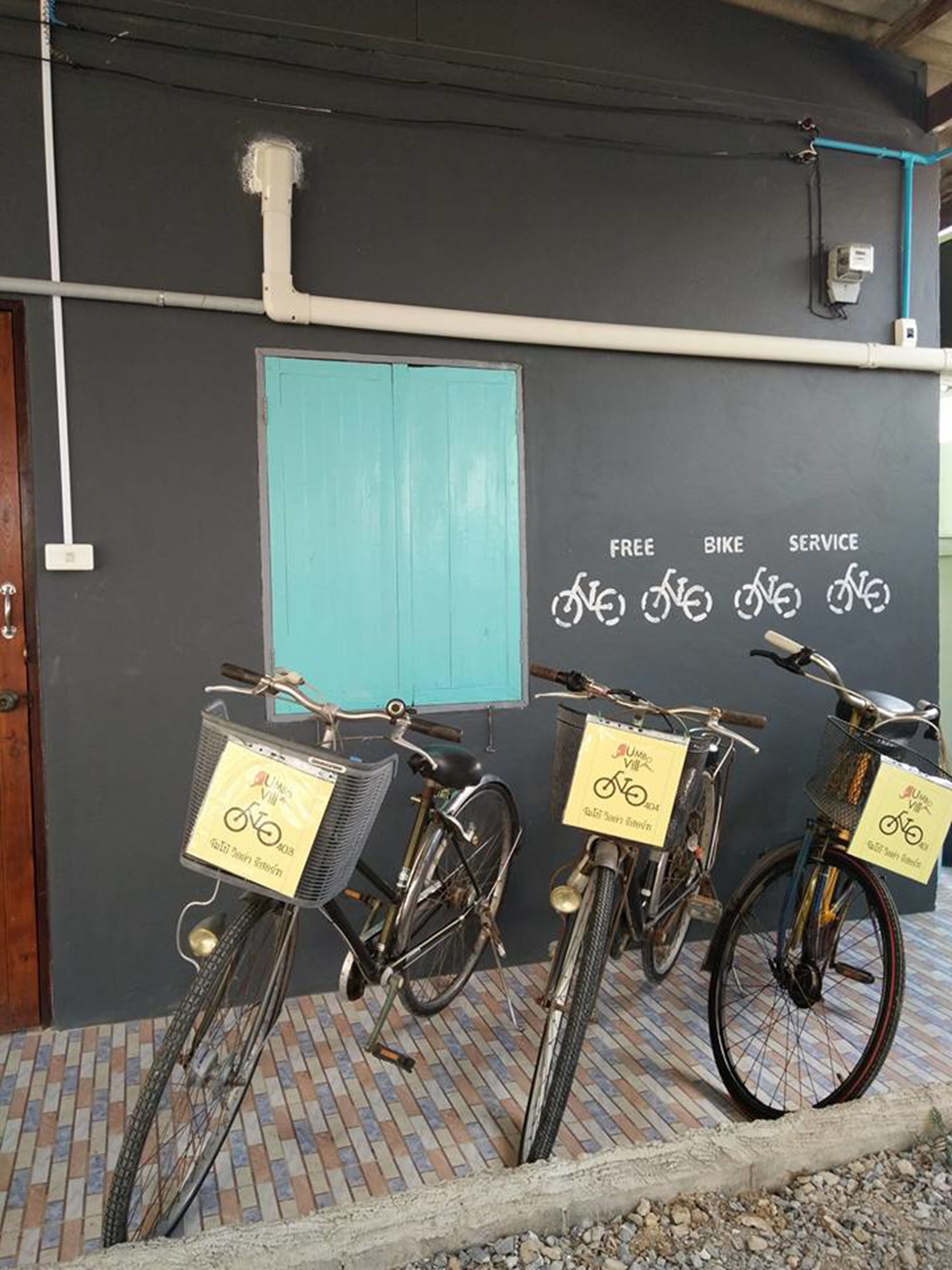 Three bicycles parked in front of a building with a blue door and a wall with text and bicycle symbols.