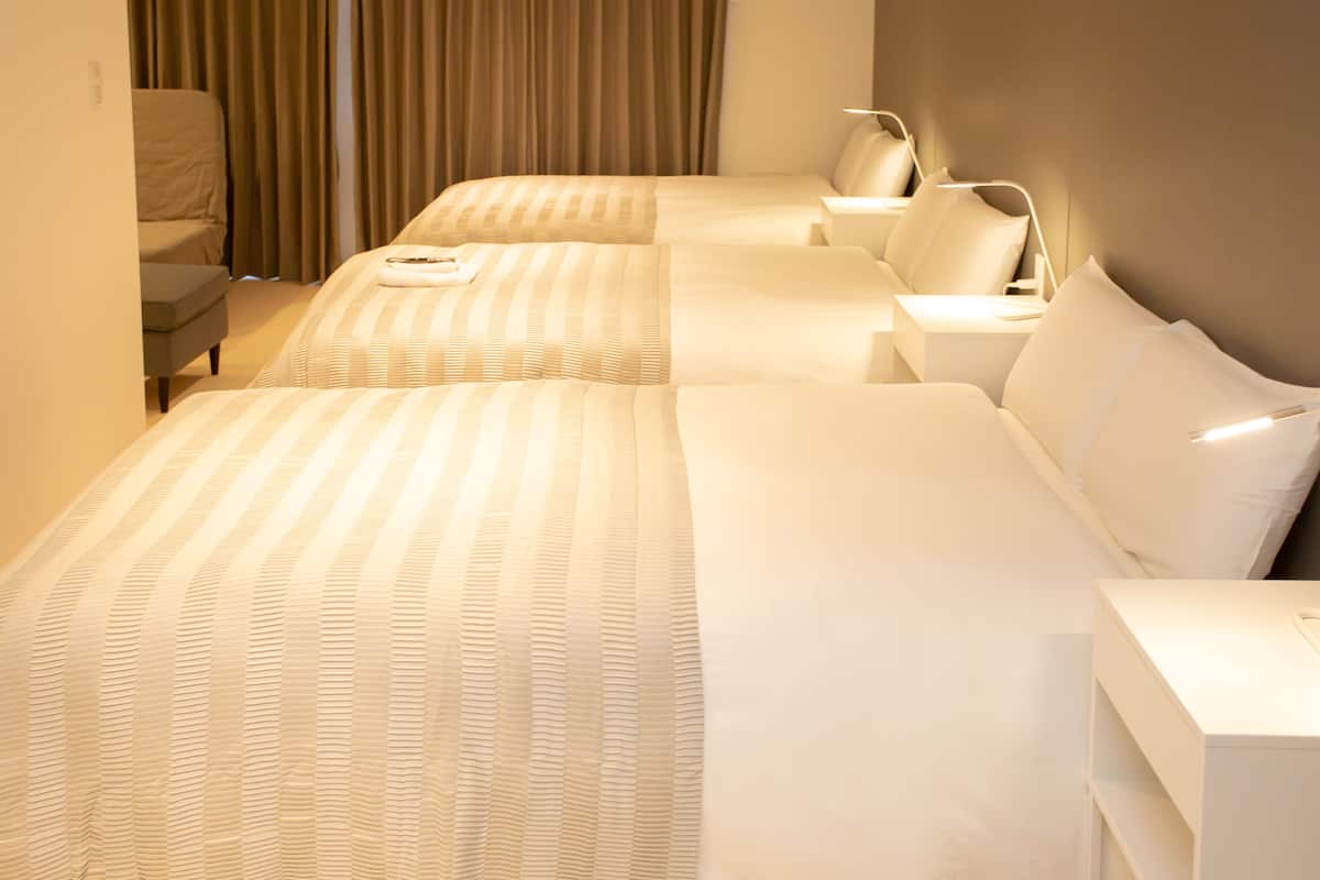 A hotel room with two beds, a chair, and a desk with a lamp.