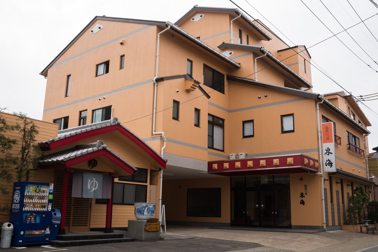 Un edificio de varios pisos con fachada roja y amarilla, una máquina expendedora y un letrero con caracteres japoneses.