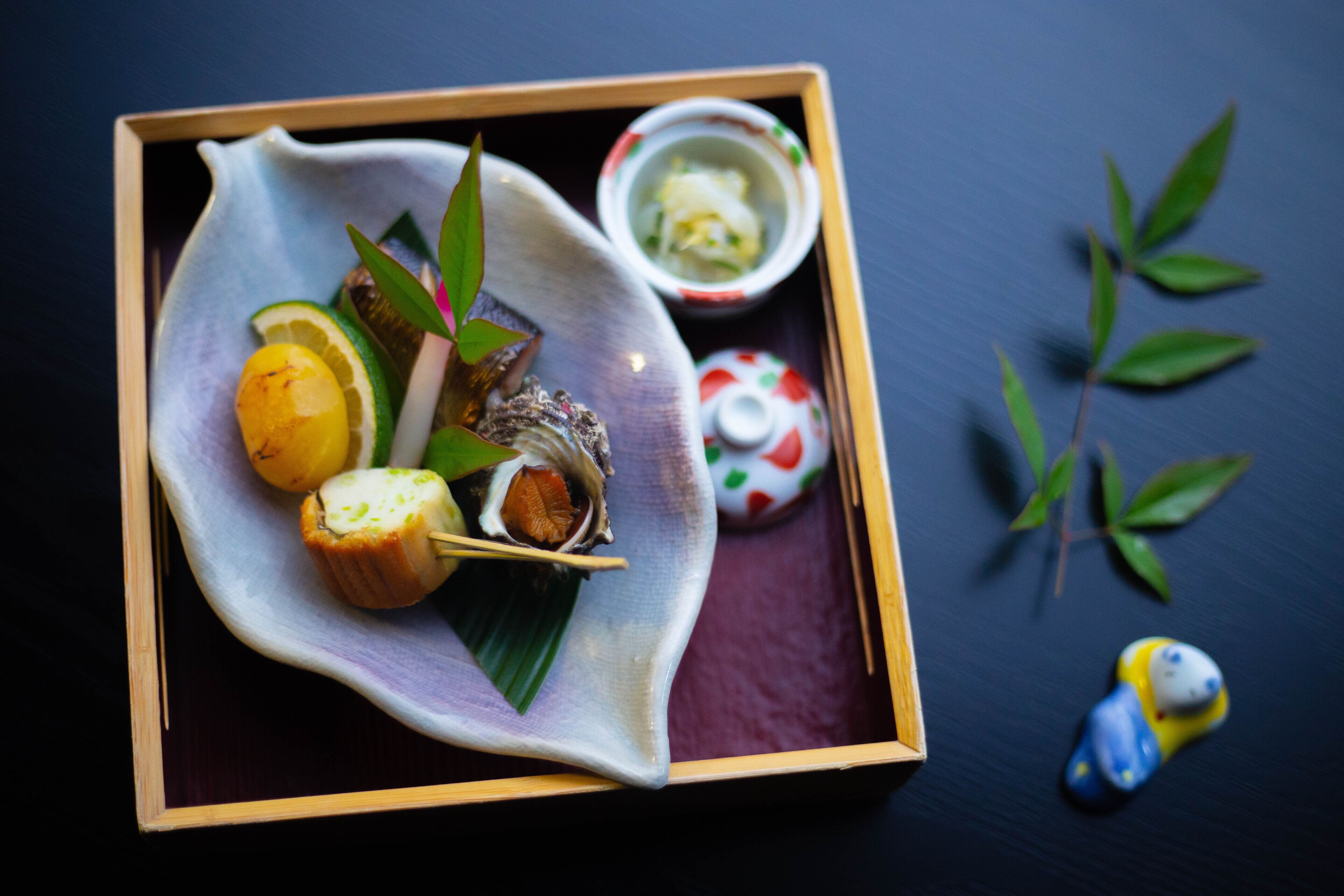 A traditional Japanese meal with sushi, a small bowl of soup, and a decorative item on a dark surface.