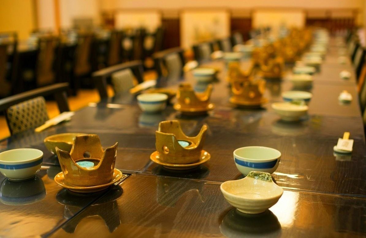 Una larga mesa de comedor con varios juegos de cuencos y un centro de mesa con forma de corona dorada.