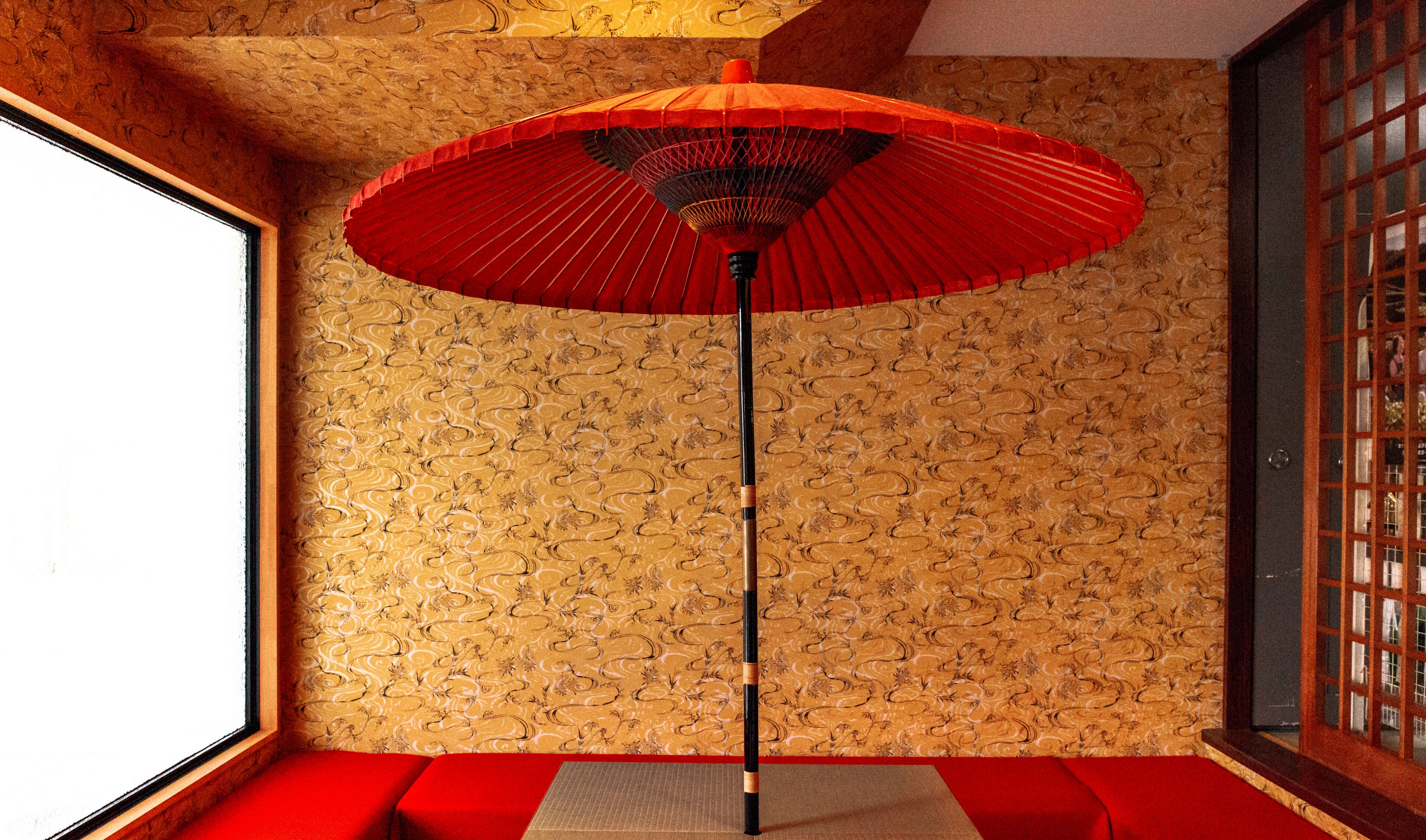Ein Zimmer mit strukturiertem Wandpapier, einem roten Sitzkissen und einem traditionellen roten Regenschirm.