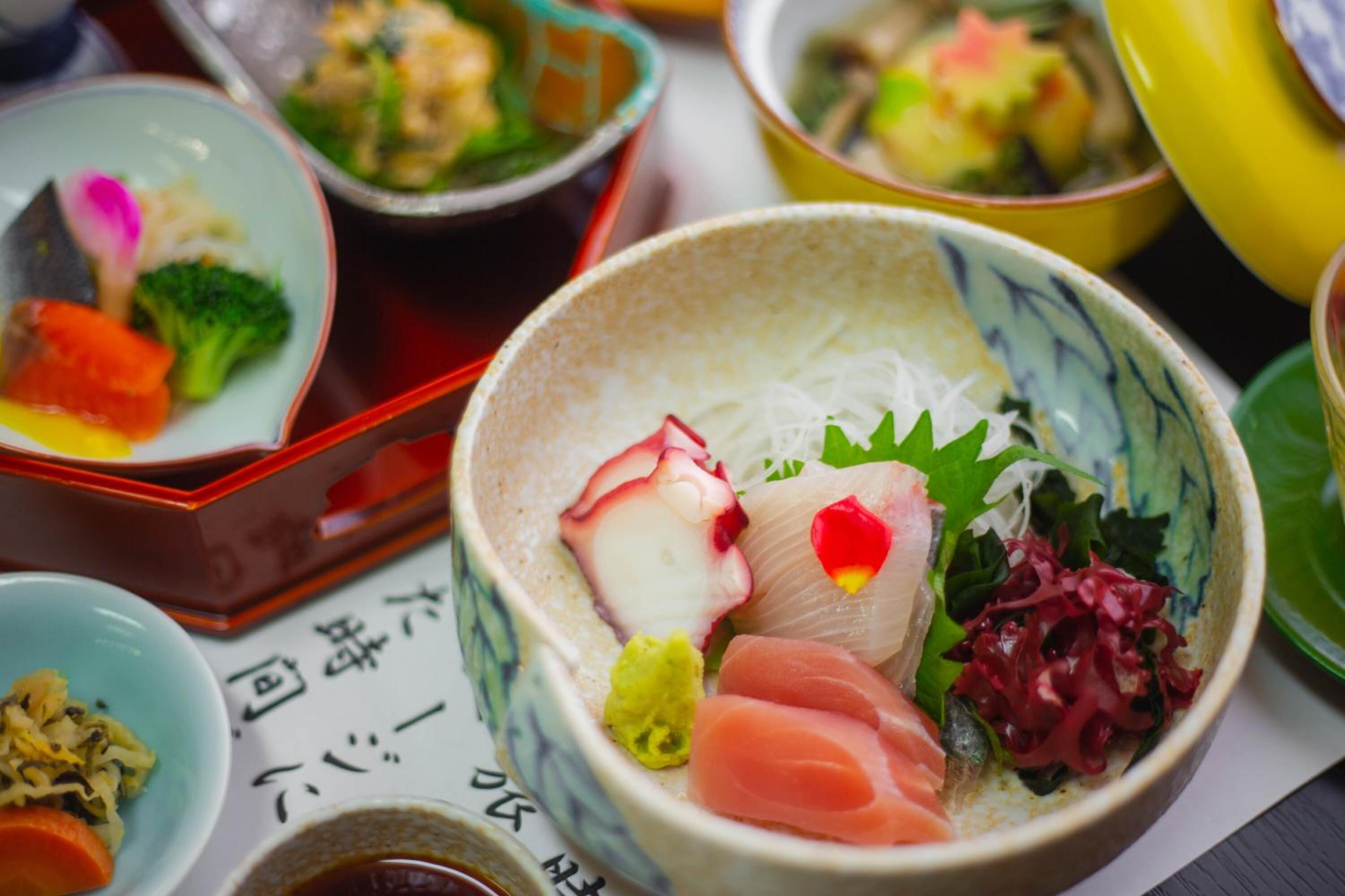 Verschiedene Gerichte in traditionellen Schüsseln, darunter Sashimi und Gemüse.