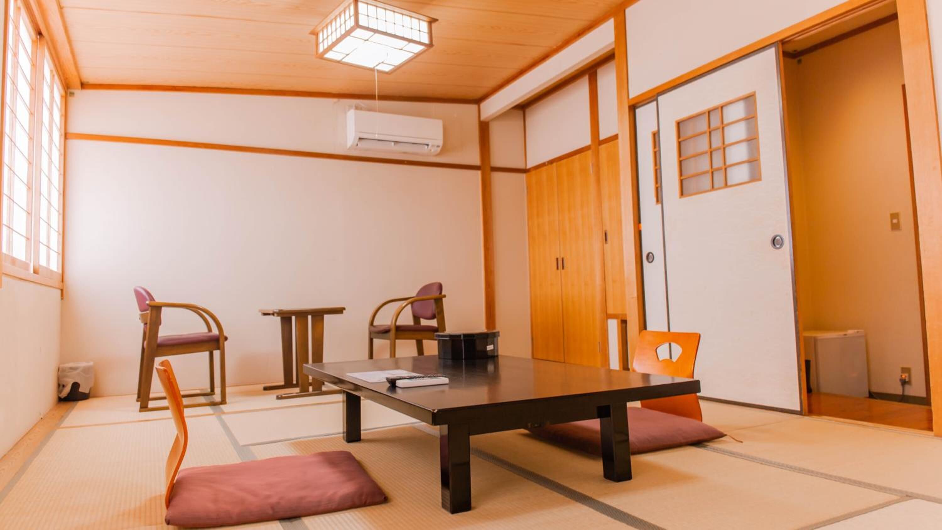 A traditional Japanese room with tatami flooring, a low table, two chairs, and a sliding door.