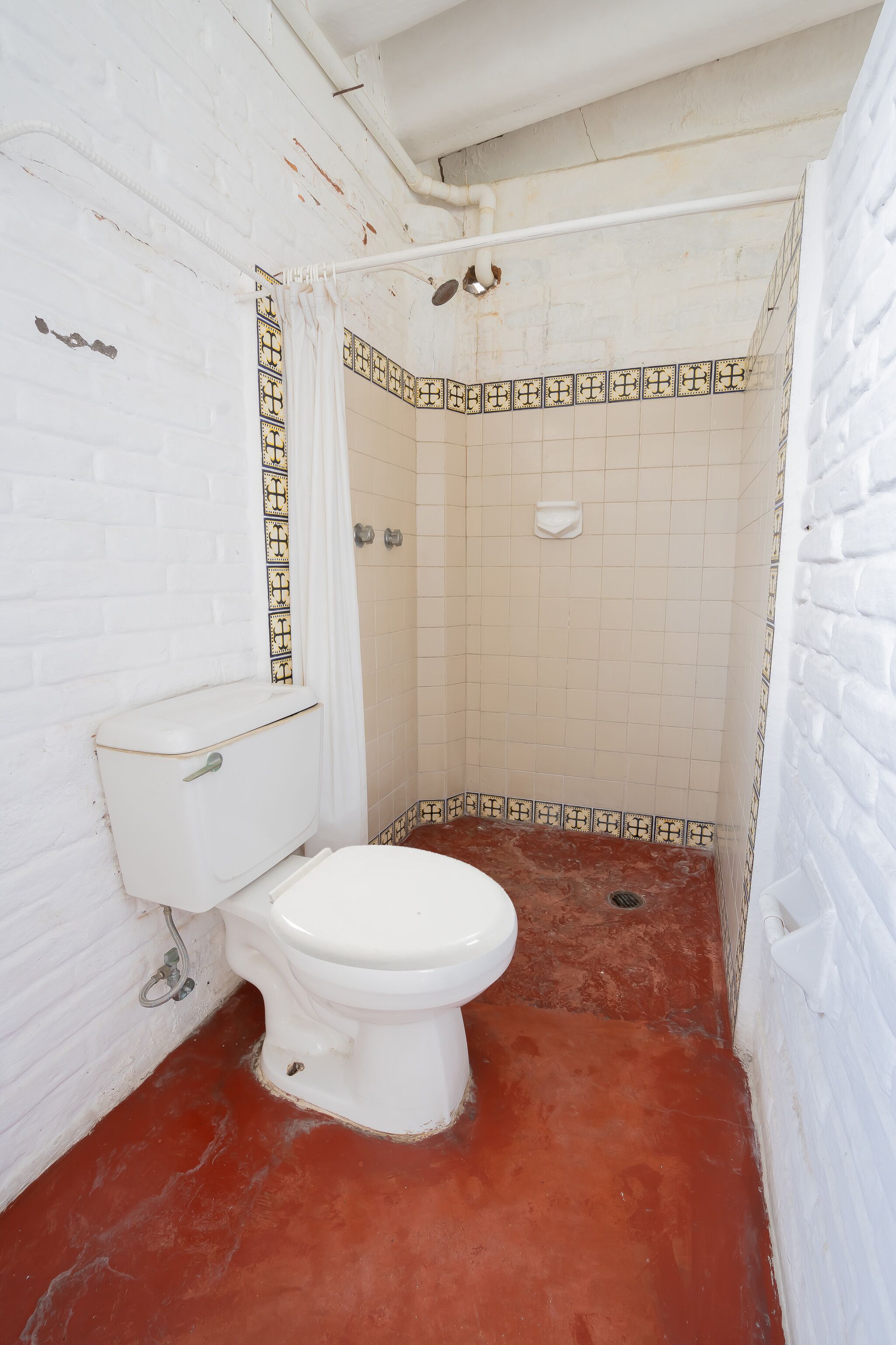 A bathroom with a white toilet, a shower area, and a red floor.