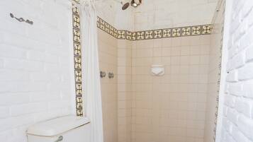 A bathroom with a white toilet, a shower area, and a red floor.