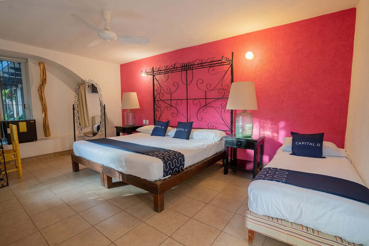 A hotel room with two beds, a large mirror, a ceiling fan, and a red accent wall.