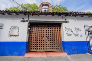 Entrada de un hotel con un portón de madera, una pequeña ventana y un cartel que indica el nombre y la ubicación del hotel.