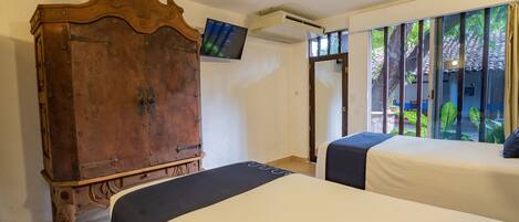 Una habitación con dos camas, un armario de madera, un ventilador de techo, un equipo de aire acondicionado y un televisor en la pared.