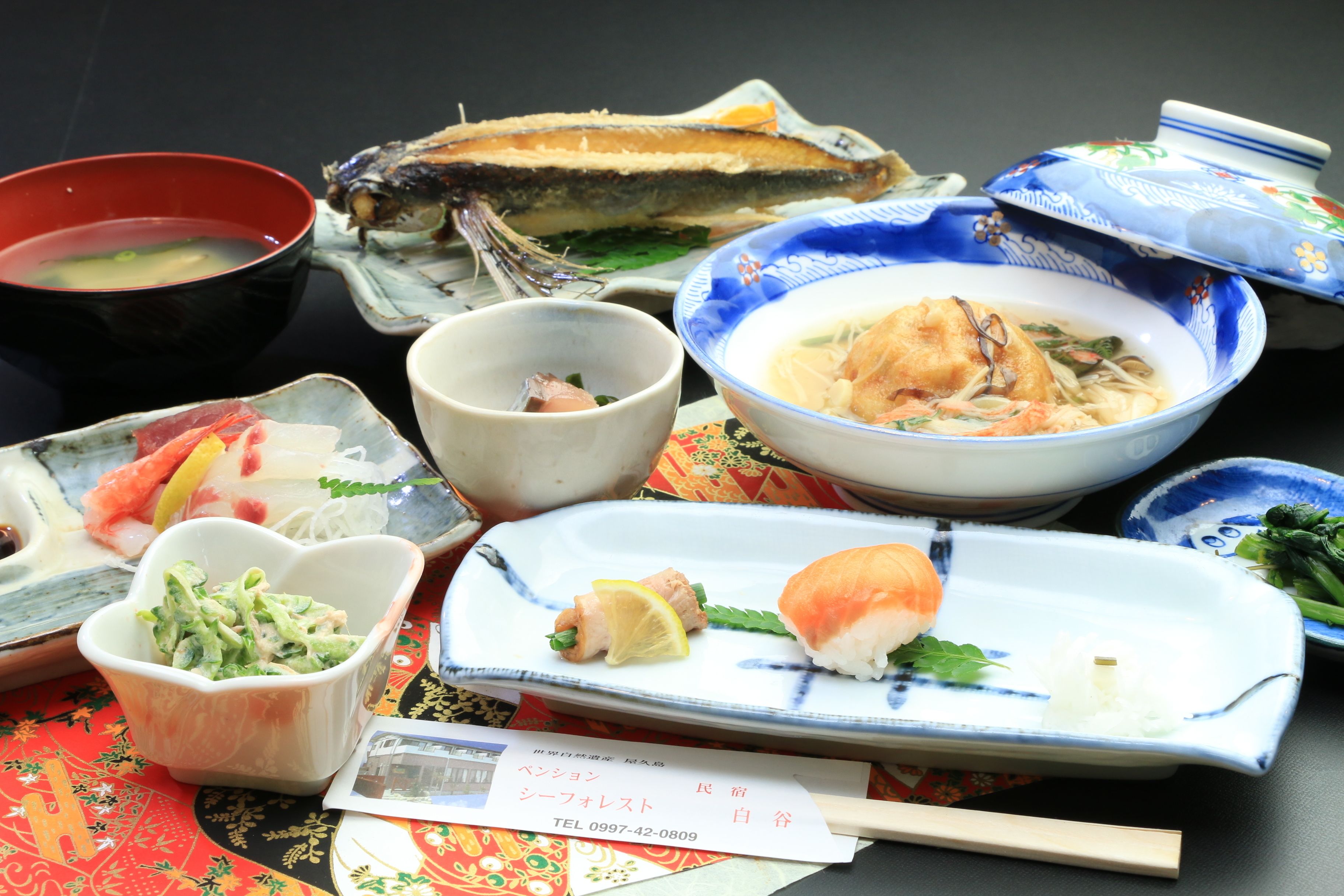 Une variété de plats japonais, notamment des sushis, des sashimis et des soupes, servis dans des assiettes et des bols traditionnels en céramique.