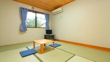 A room with tatami flooring, a wooden table, blue cushions, a television, and a window with blue curtains.