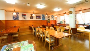 A restaurant with wooden tables and chairs, a menu on the table, and artwork on the walls. - Pension Sea Forest (Yakushima)