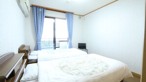 A hotel room with two beds, a desk, a chair, a television, and a window with curtains. - Pension Sea Forest (Yakushima)