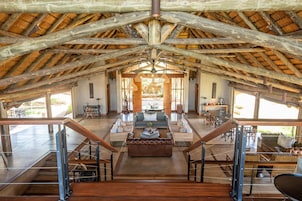 Un amplio espacio tipo loft con techo alto y vigas de madera a la vista, un área de estar central con sofá y mesa de centro, y una escalera que conduce a un nivel superior.