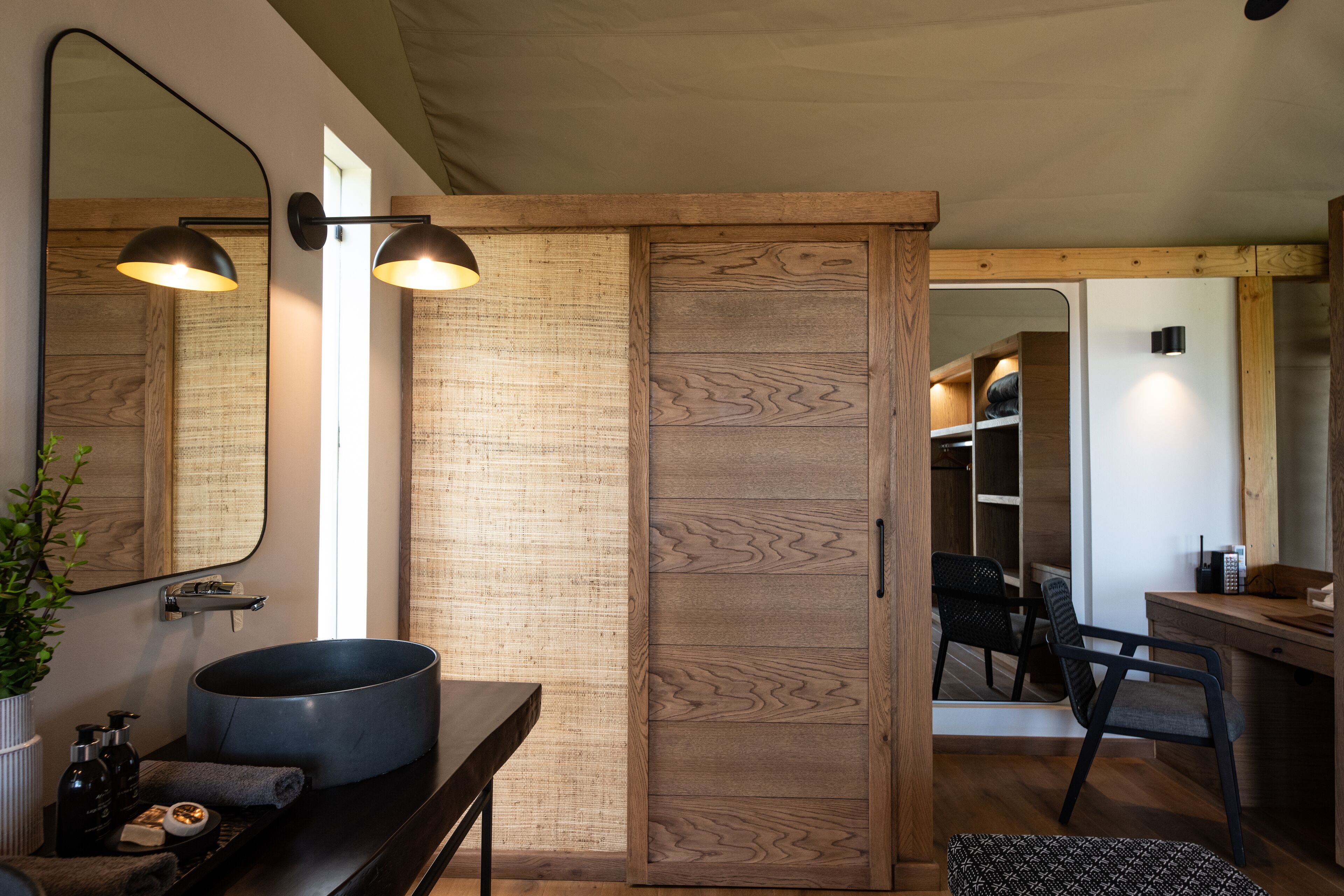 A modern bathroom with a large mirror, two pendant lights, a round sink, and a wooden vanity.